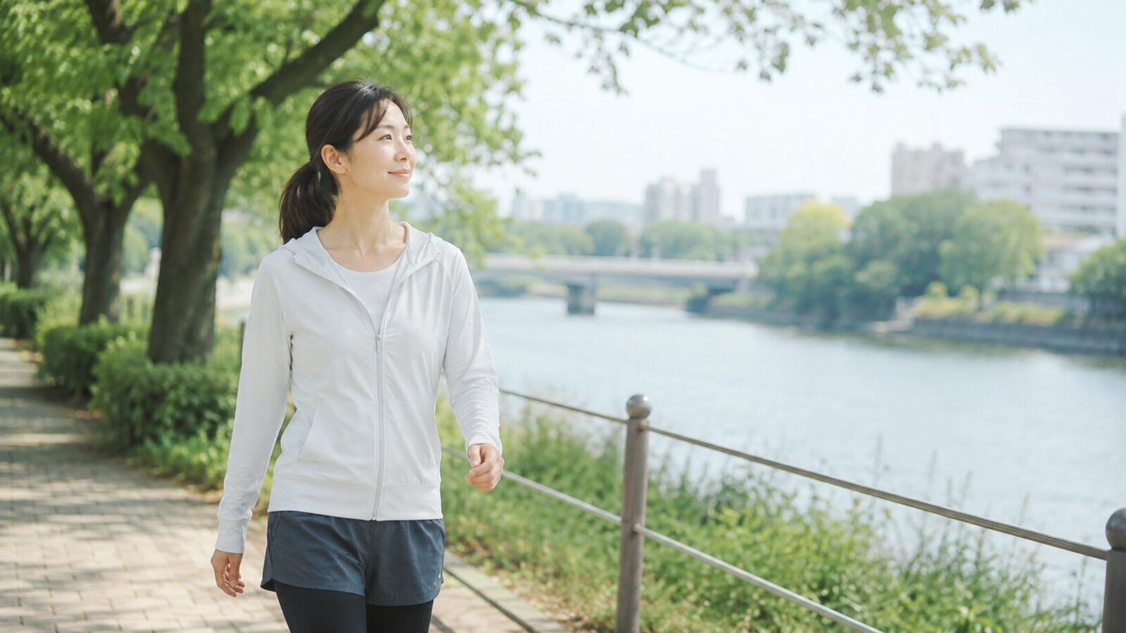 川沿いをウォーキングしながら肩こり対策として体を動かしている女性のイメージ画像